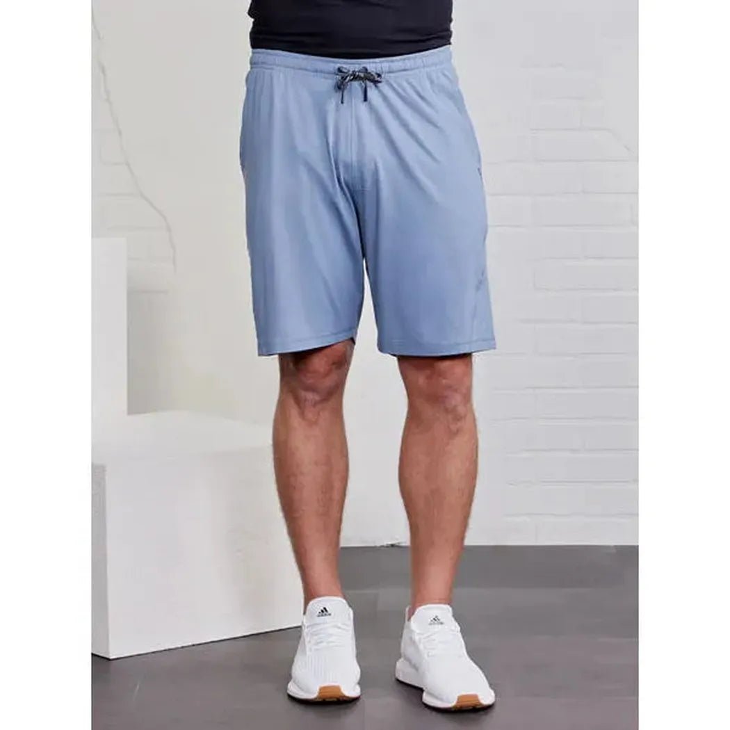 A front view of the Tasc Men's Carrollton Classic Short in Anchor color on a model wearing white sneakers against a white brick wall background.