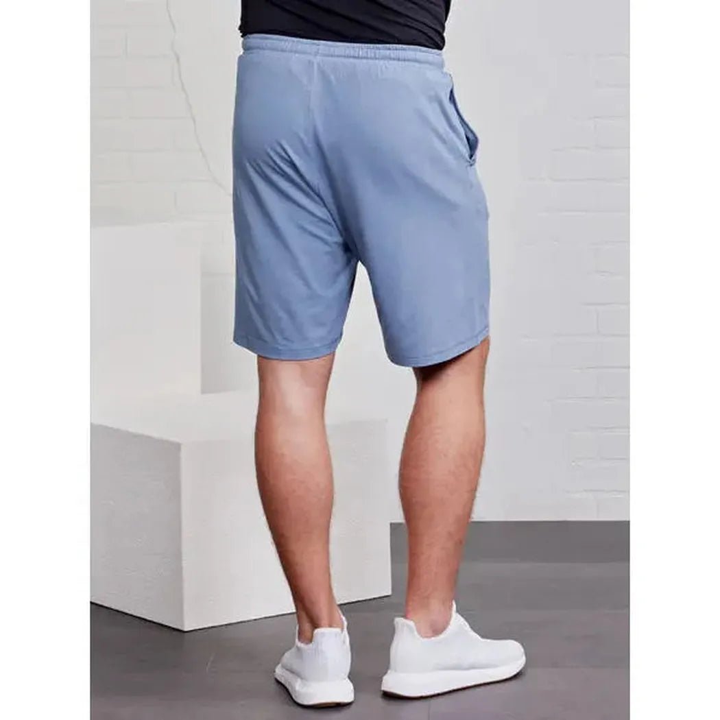 Back view of the Tasc Men's Carrollton Classic Short in Anchor, showing the model wearing white sneakers against a white brick background.