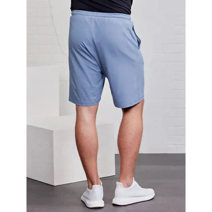 Back view of the Tasc Men's Carrollton Classic Short in Anchor, showing the model wearing white sneakers against a white brick background.