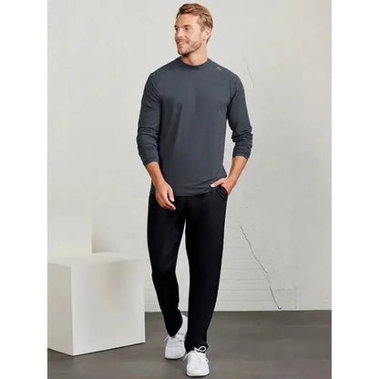 A man wearing the Tasc Men's Carrollton Long Sleeve in Iron Heather stands with one hand in his pocket against a light gray wall.