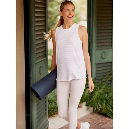 A woman wearing the Tasc Women's Nola Tank 2.0 in Heritage Blue walks outside near green shutters.