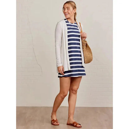 A woman wearing the Tasc Women's Summer Tank Dress Stripe in Classic Navy White stands against a light background with a woven bag.