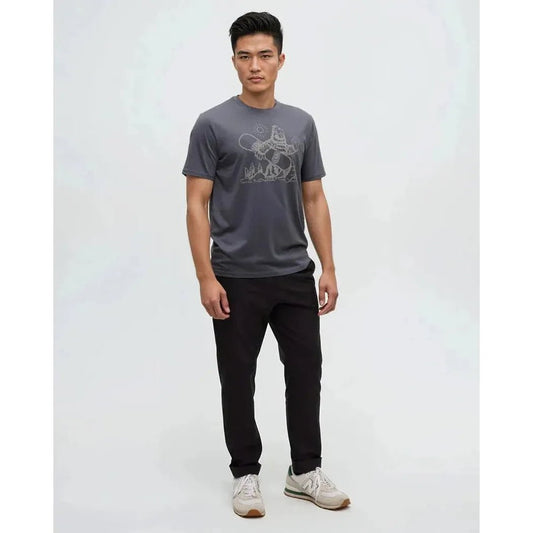 A model wearing the Tentree Men's Sasquatch Sends It T-Shirt in Graphite Paloma Grey stands against a plain white background.