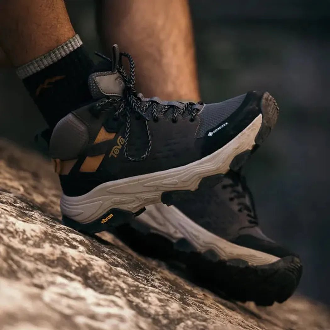 A close-up side view of the Teva Men's Grandview Max GTX in Charcoal/Black on a rocky surface.