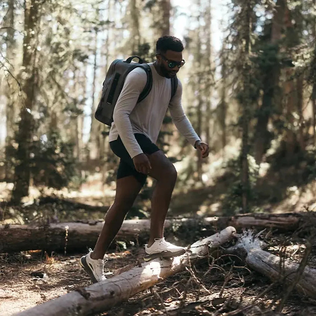 A man in Unexplored/ Vapor Blue Teva Men's Trailwinder Low shoes steps on a log in a forest.