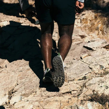A man in Unexplored/ Vapor Blue Teva Men's Trailwinder Low shoes walks on rocky terrain from behind.