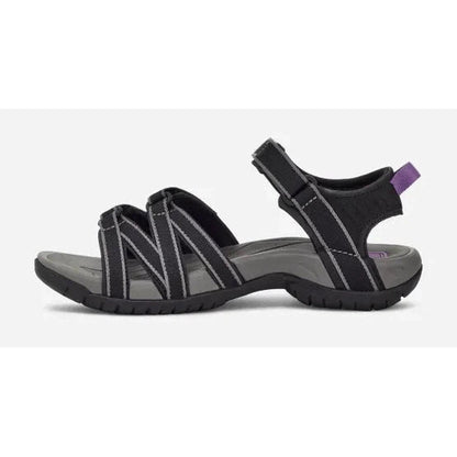 Side view of the Teva Women's Tirra in Black/Grey showing the adjustable strap and purple pull tab against a white background.