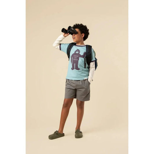 A young model wearing The Landmark Project Leave No Trace Youth Short Sleeve Ringer Tee in Glacier Blue/Dusk looks through binoculars against a neutral background.