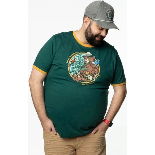 A man wearing The Landmark Project Smokey's Friends Ringer Tee in Spruce + Golden stands with his hands in his pockets against a white background.