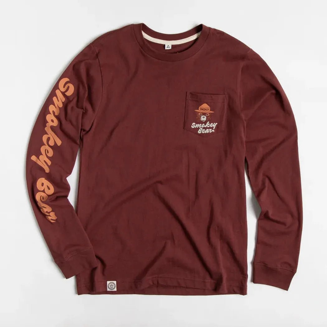 A front view of the Angostura The Landmark Project Spark A Change Unisex Long Sleeve Tee w/ Pocket with a pocket on the chest and text on the sleeve against a white background.