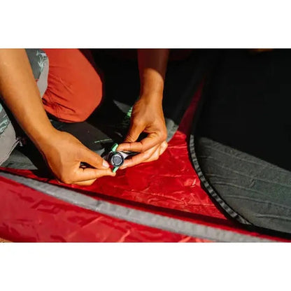 A person kneels inside a red tent, adjusting the valve on a Therm-a-Rest Trail Scout sleeping pad.