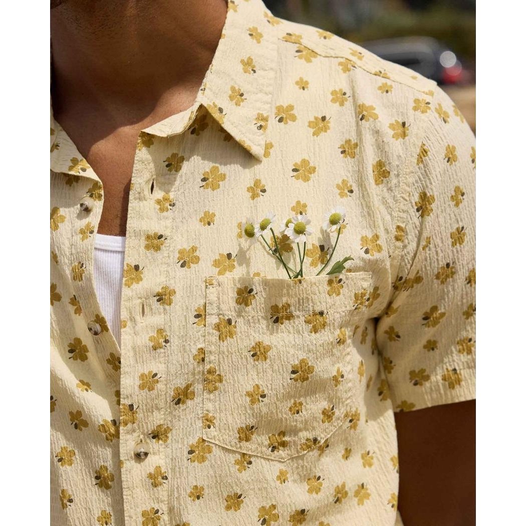 A close-up of the Toad & Co Men's Fletcher Short Sleeve Shirt in Barley Pattern, showing the pocket with small flowers and a white undershirt, against an outdoor background.