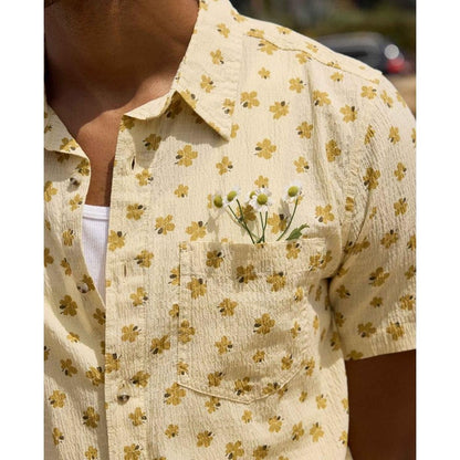 A close-up of the Toad & Co Men's Fletcher Short Sleeve Shirt in Barley Pattern, showing the pocket with small flowers and a white undershirt, against an outdoor background.