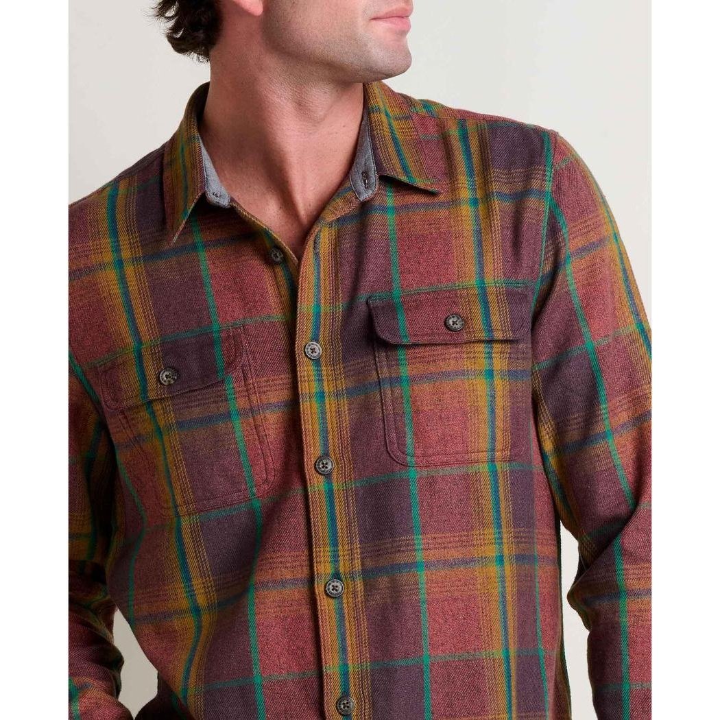 A man wears the Toad & Co Men's Ranchero Long Sleeve Shirt in Cinnamon with a plaid pattern, showing the front pockets and button closure against a plain background.