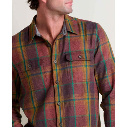 A man wears the Toad & Co Men's Ranchero Long Sleeve Shirt in Cinnamon with a plaid pattern, showing the front pockets and button closure against a plain background.