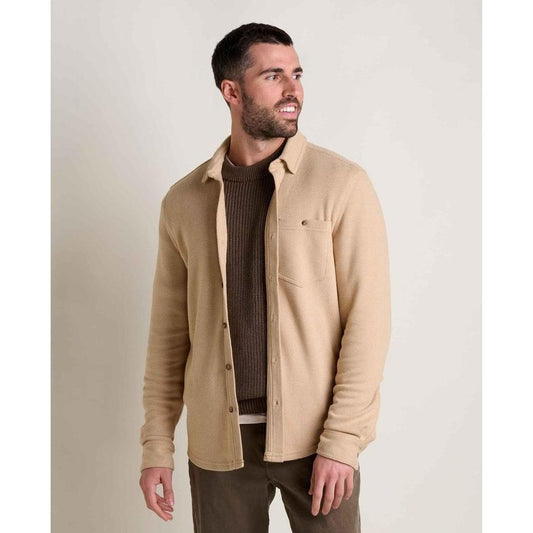 A man wearing the Toad & Co Men's Shadowbrook Long Sleeve Shirt in Camel Twill stands against a plain background.