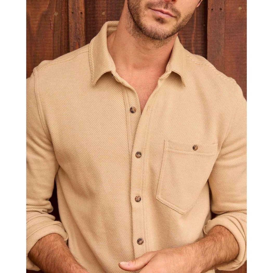 A front view of the Toad & Co Men's Shadowbrook Long Sleeve Shirt in Camel Twill on a model against a wooden background.