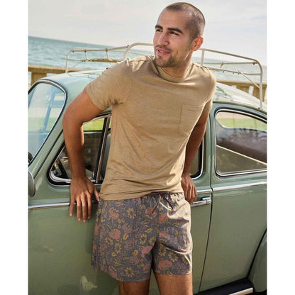 A man in a khaki Toad & Co Men's Tempo Short Sleeve Pocket Crew leans against a vintage car by the ocean.