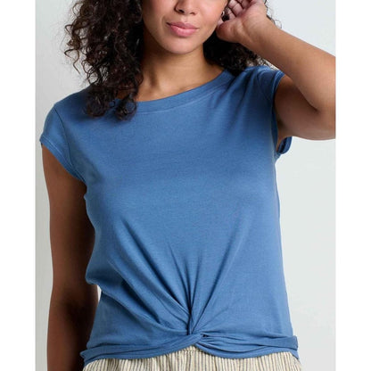 A woman wearing the Toad & Co Women's Anza Short Sleeve Shirt in Pacific Blue, with a knotted hem, against a light background.