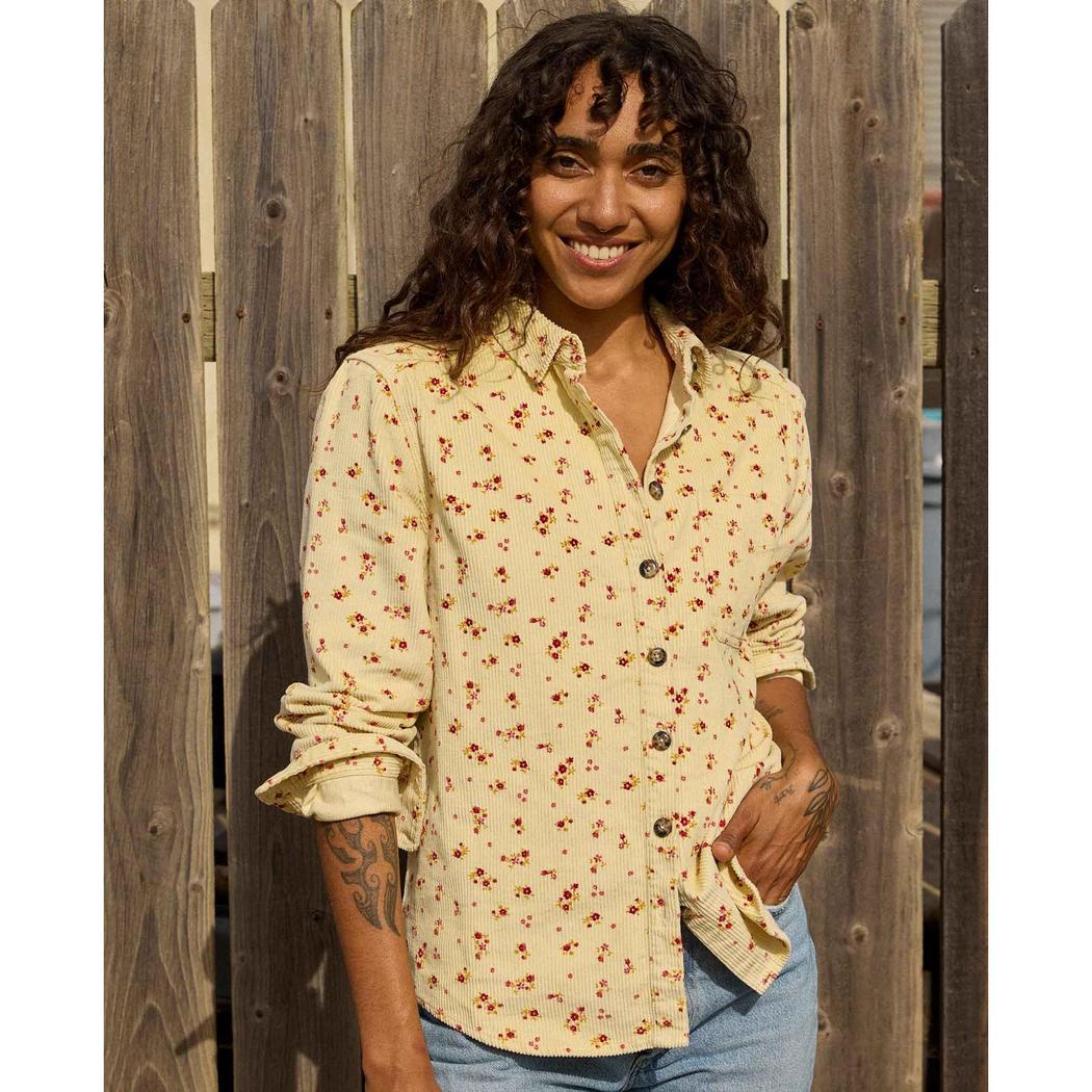 A woman wearing the Toad & Co Women's Cascadia Long Shirt in Barley Floral Print stands in front of a wooden fence.