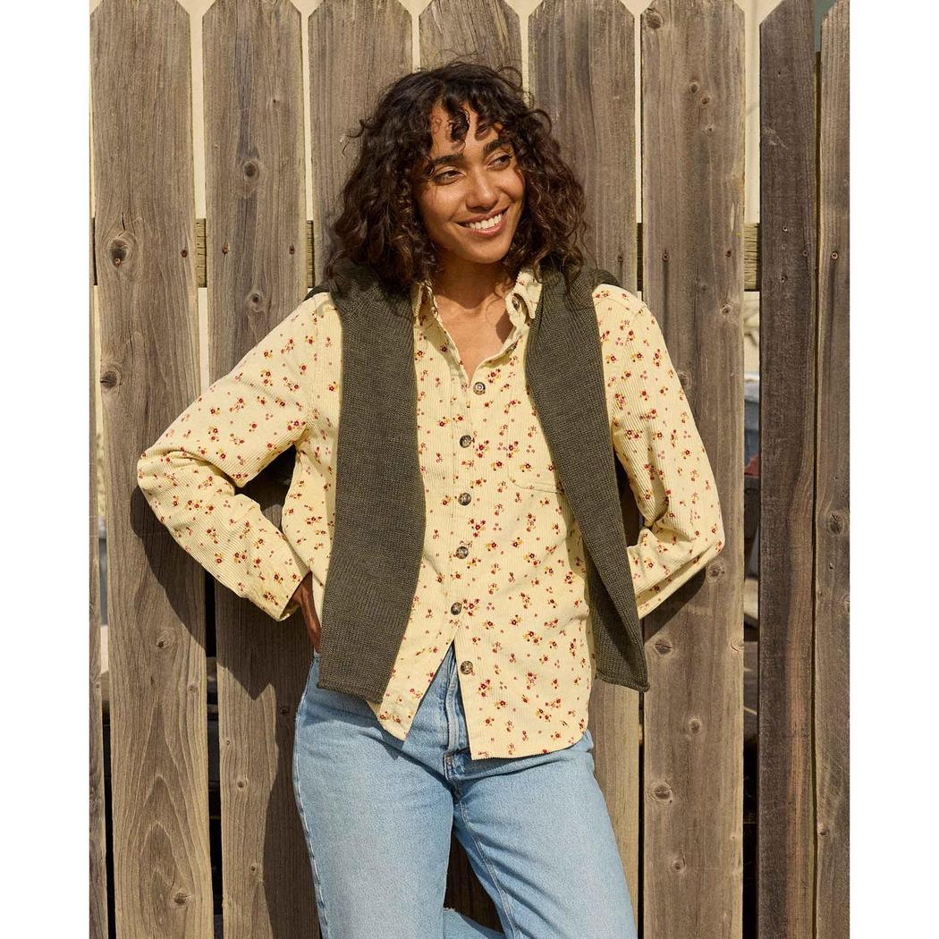 A woman wearing the Toad & Co Women's Cascadia Long Shirt in Barley Floral Print poses in front of a wooden fence.