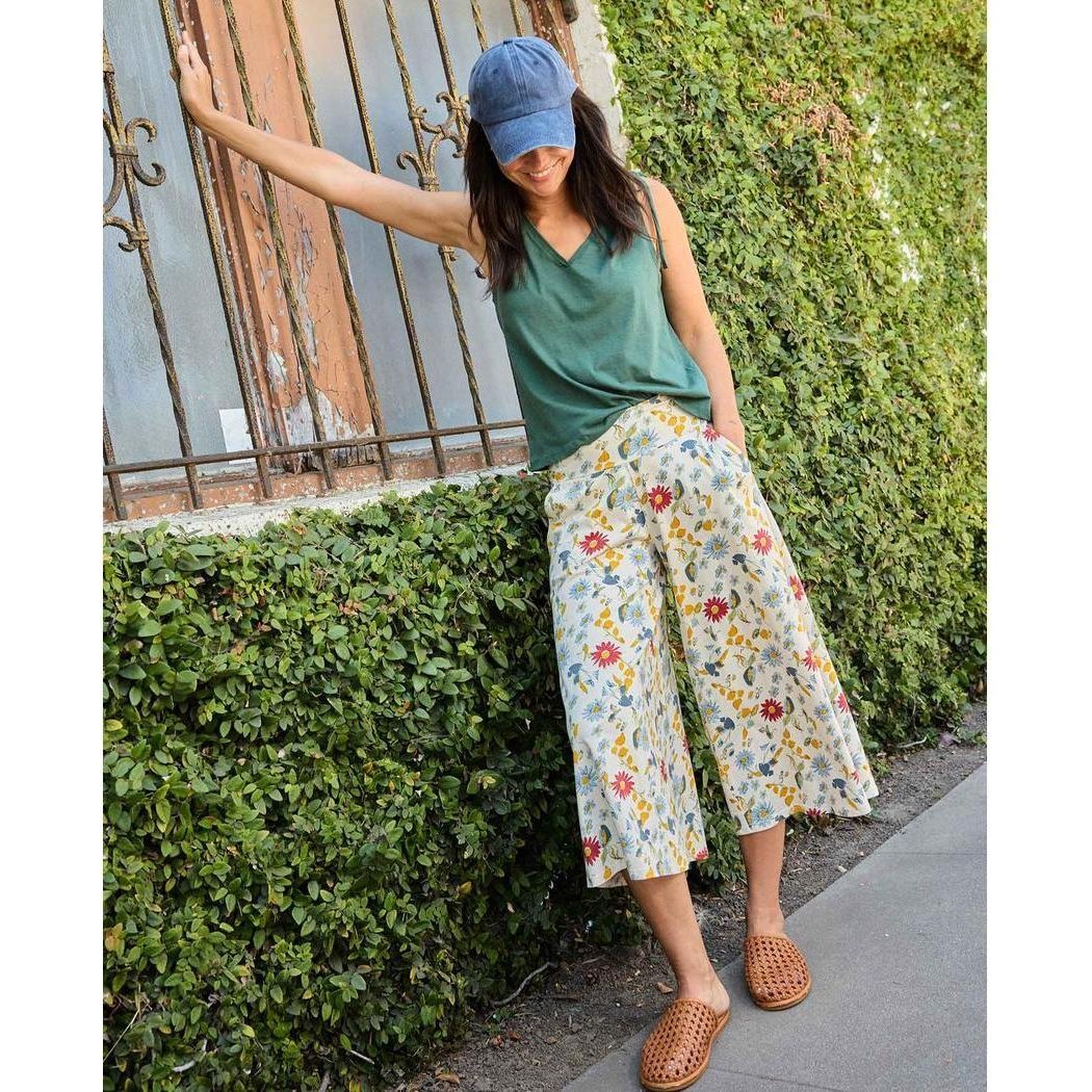 A woman wearing Toad & Co Women's Chaka Culotte in Almond Print poses outdoors near a hedge and window.