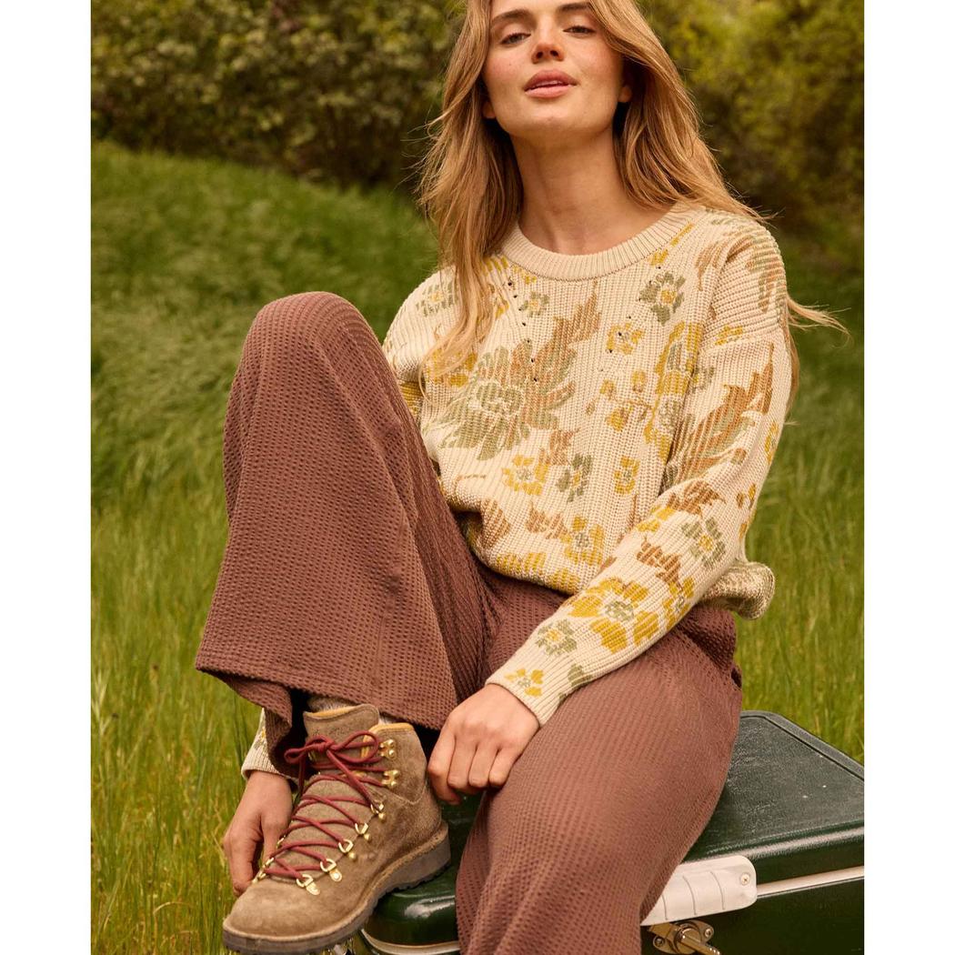 A woman wearing Toad & Co Women's Chaka Wide Leg Pant in ChestnutTexture sits on a suitcase in a grassy outdoor setting.