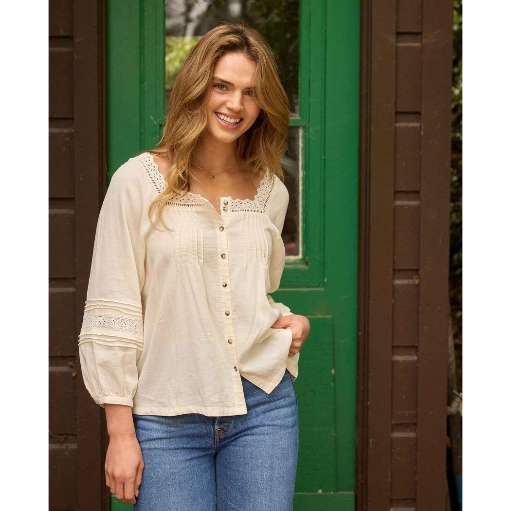A woman wearing the Toad & Co Women's Manzana Peasant LS Shirt in Egret stands in front of a green door.