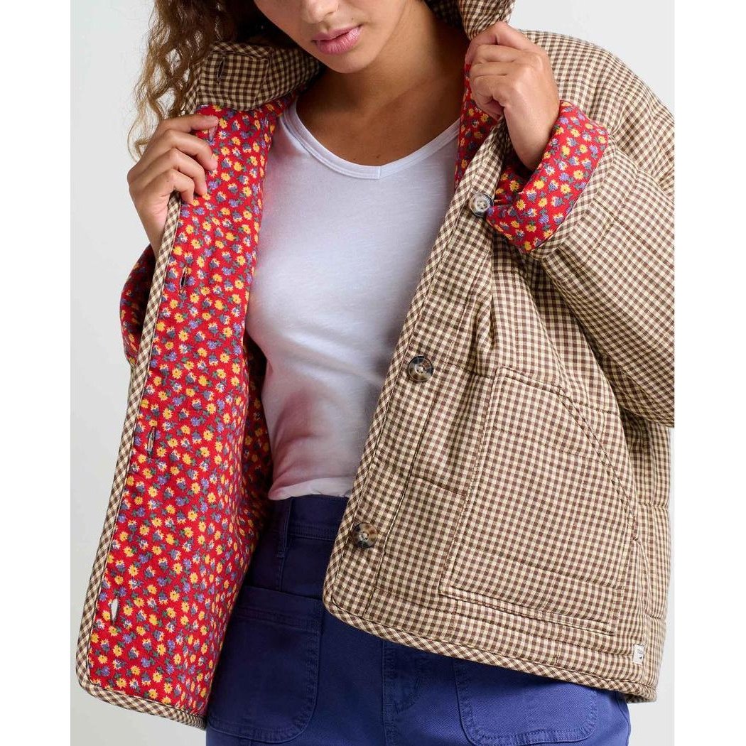 A woman wearing the Toad & Co Women's Manzana Quilted Jacket in Partridge Gingham holds the collar, showing the colorful floral lining against a plain background.