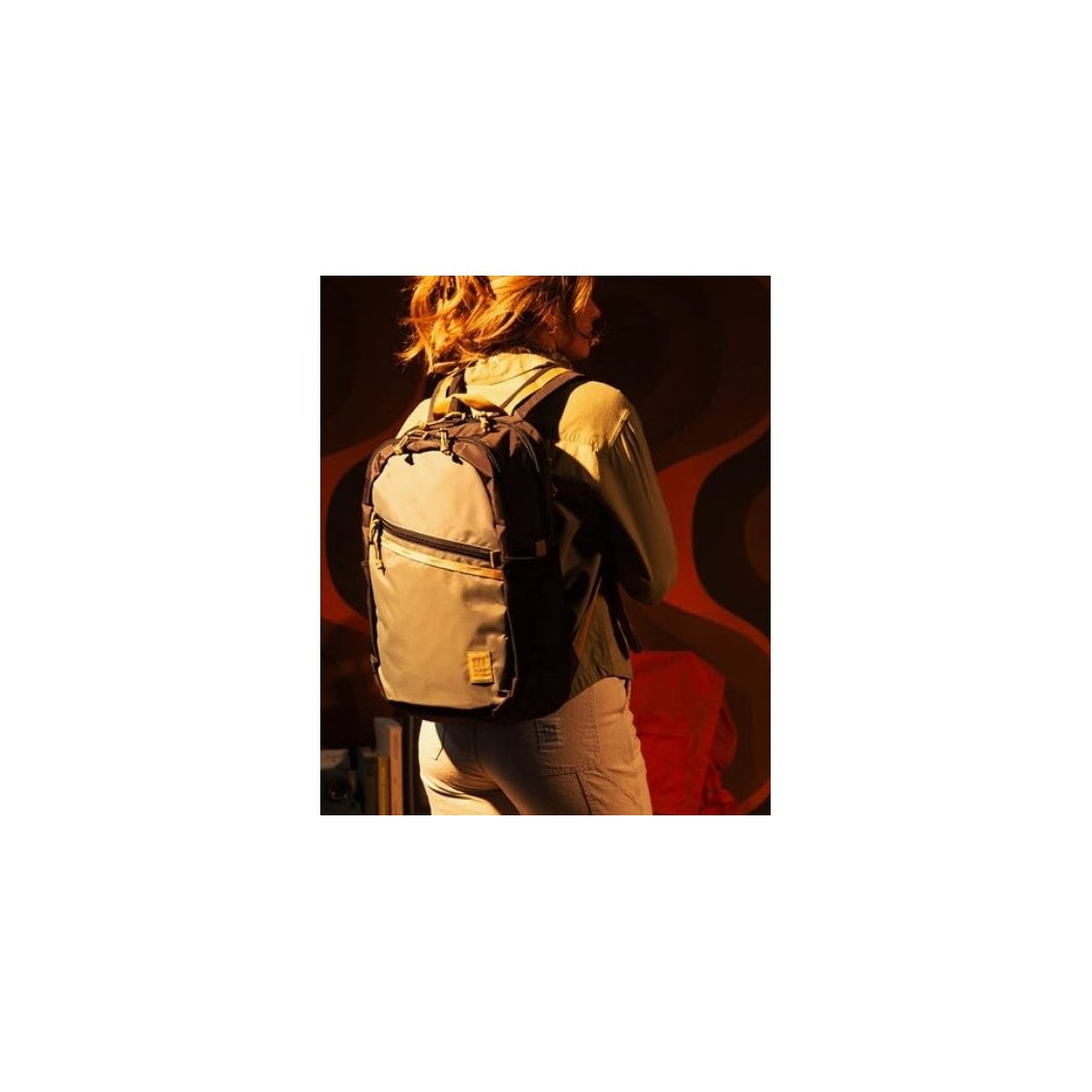 Back view of the Topo Designs Commuter Backpack in Beetle/Khaki on a model against a red and black background.