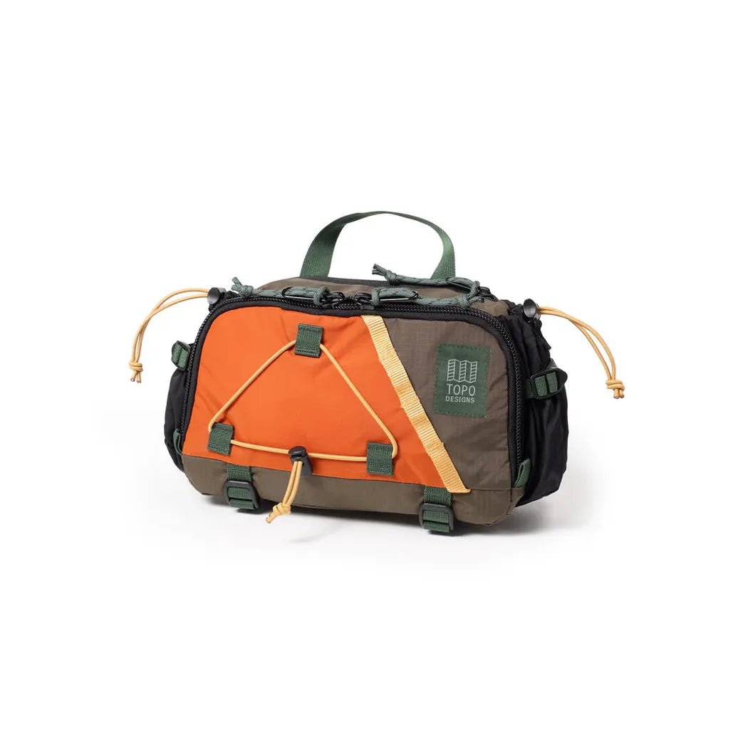A front view of the Topo Designs Mountain Hydro Hip Pack in Black/Neutral with a green top handle and orange front panel against a white background.