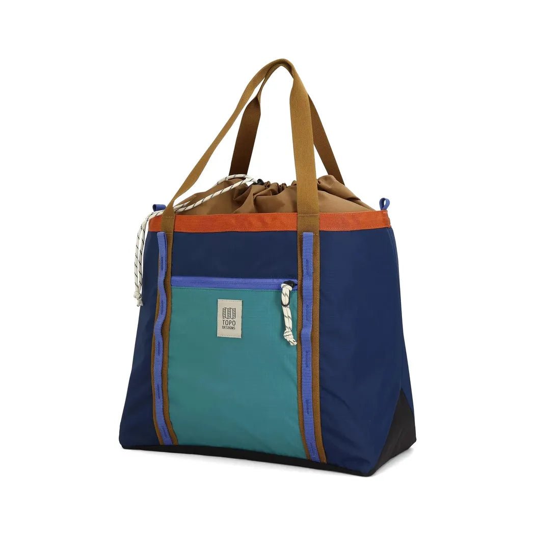 A front view of the Topo Designs Mountain Utility Tote in Forest / Bone White with a front pocket and brown straps against a white background.