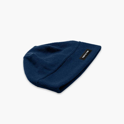 A front view of the Turtle Fur Chelonia 150 Fleece Beanie in Black with a small brand tag on the side against a white background.