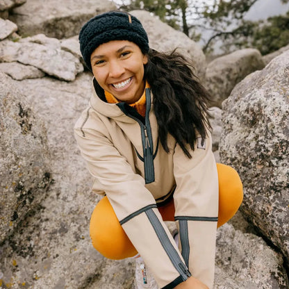 A woman wearing the Turtle Fur Comfort Lush Full Send Wide Band in Black smiles while crouching on rocky terrain.