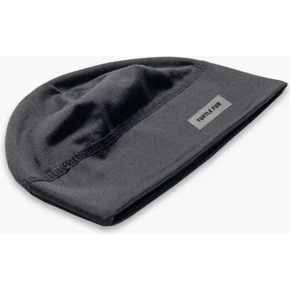 A black Turtle Fur Comfort Shell Brain Shroud beanie with a label, shown from a top-down angle on a white background.