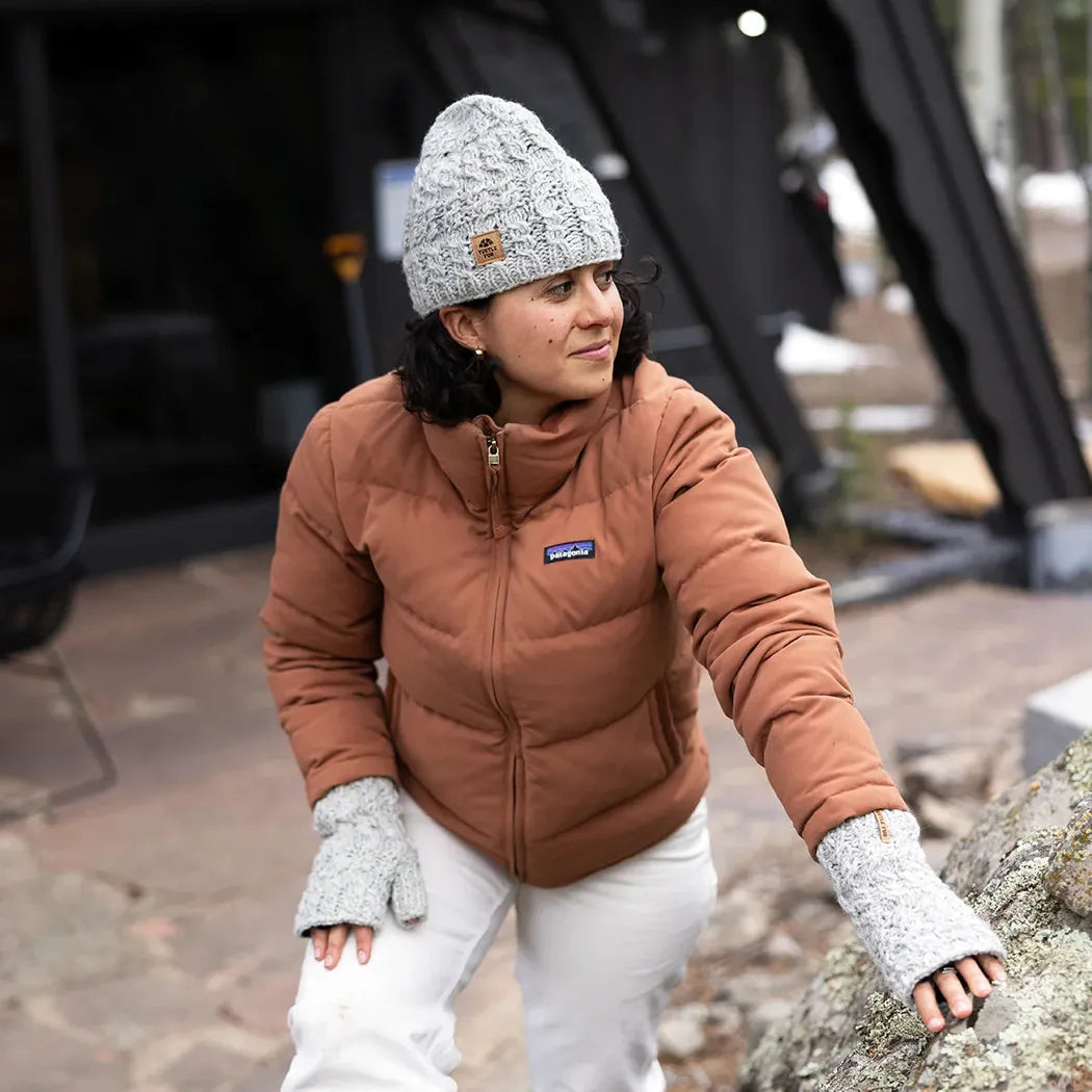 A woman wears the black Turtle Fur Nepal Handmade Wool Mika hat and matching gloves while outdoors near a rock.