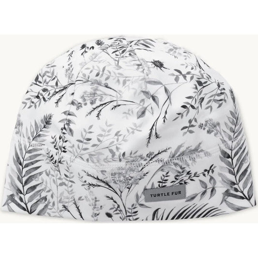 A top-down view of the Turtle Fur Women's Comfort Shell Brain Shroud in PowderDayFronds with a botanical print and a small tag.