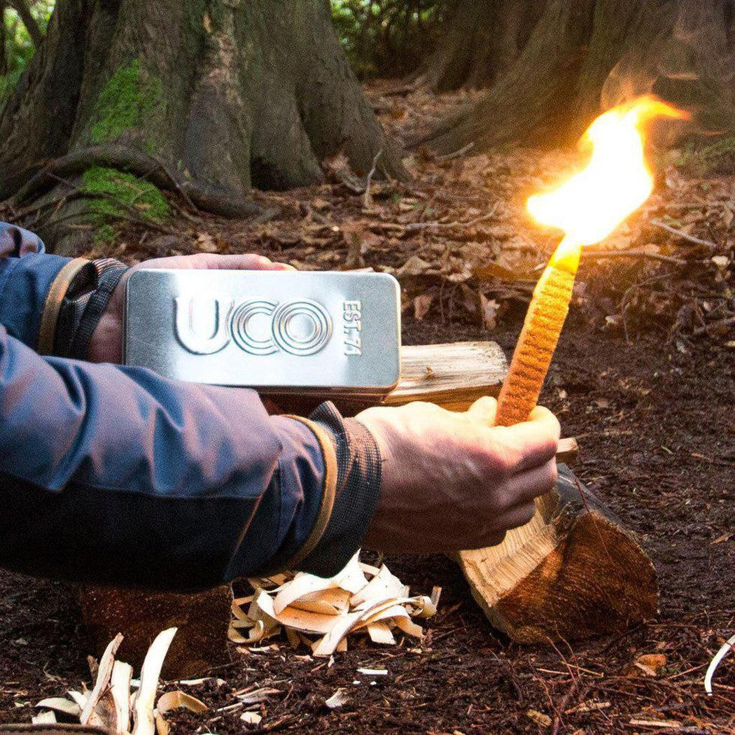 A person holds the UCO Behemoth Sweetfire Match Kit while lighting a torch in a forest setting.