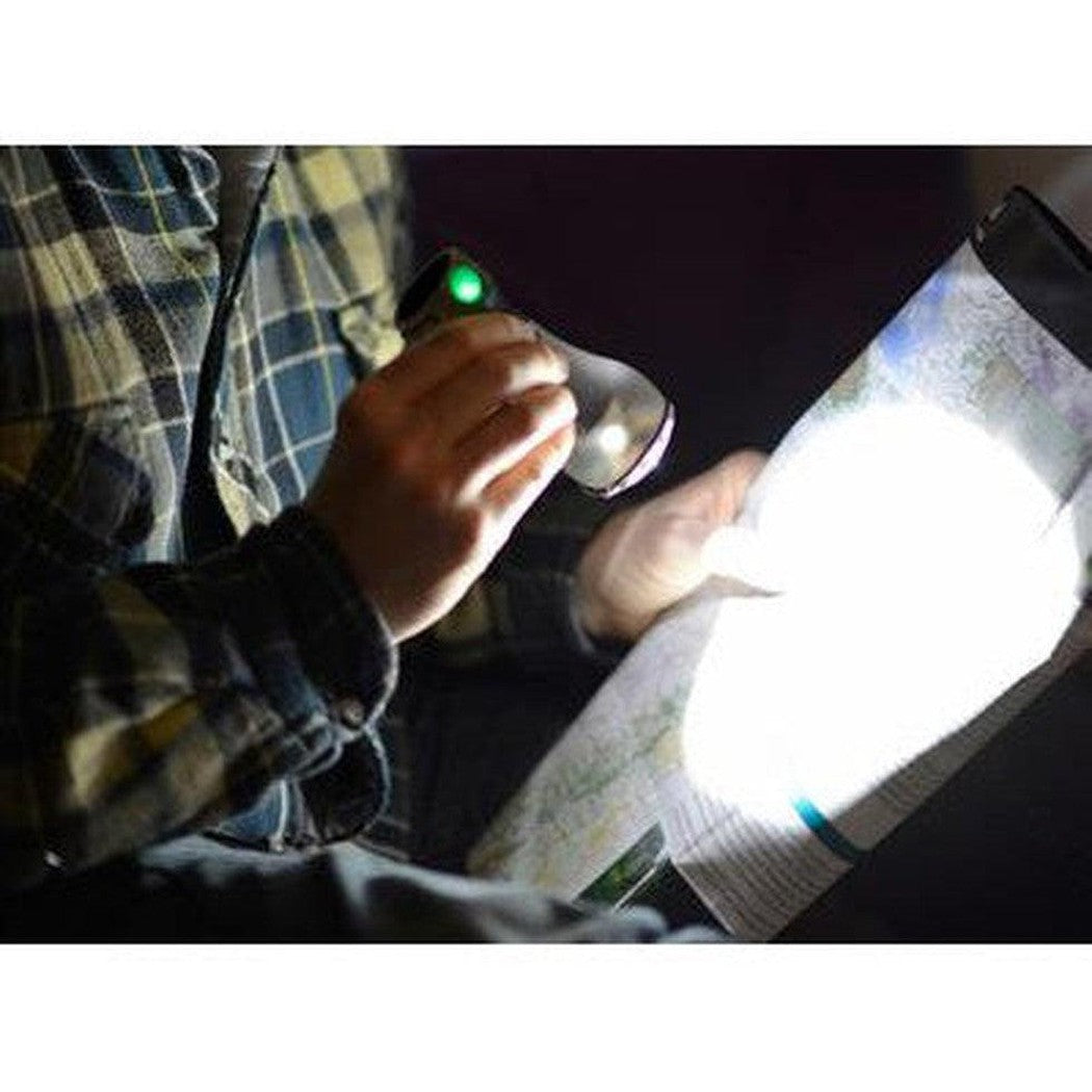 A person in a plaid shirt holds the UCO Pika LED Lantern, shining its light on a map in a dark setting.