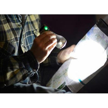 A person in a plaid shirt holds the UCO Pika LED Lantern, shining its light on a map in a dark setting.