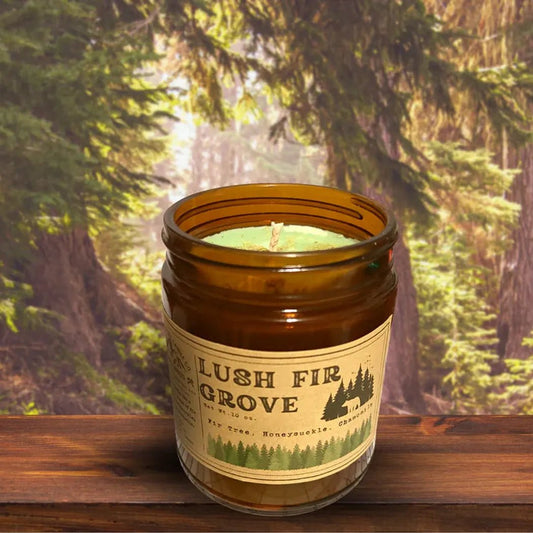 A 4 oz Wanderlust Folk Lush Fir Grove candle sits on a wooden surface with a forest background.