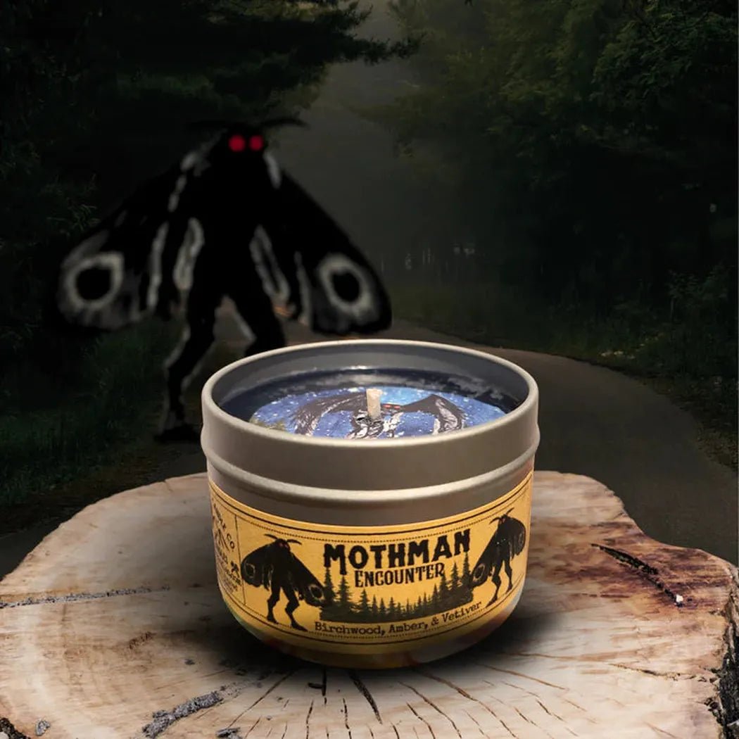 A 4 oz Wanderlust Folk Mothman Encounter candle sits on a tree stump with a dark forest background.