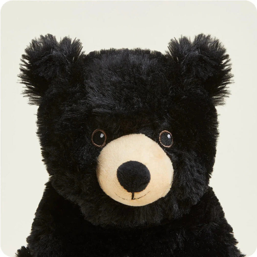 A close-up front view of the Warmies Bear with its black fur and cream-colored snout against a plain light background.