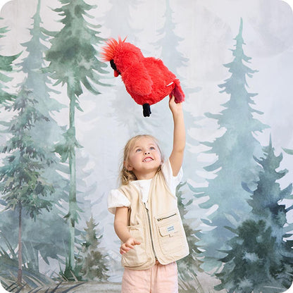 A young girl holds up the Warmies Cardinal plush toy against a forest backdrop.