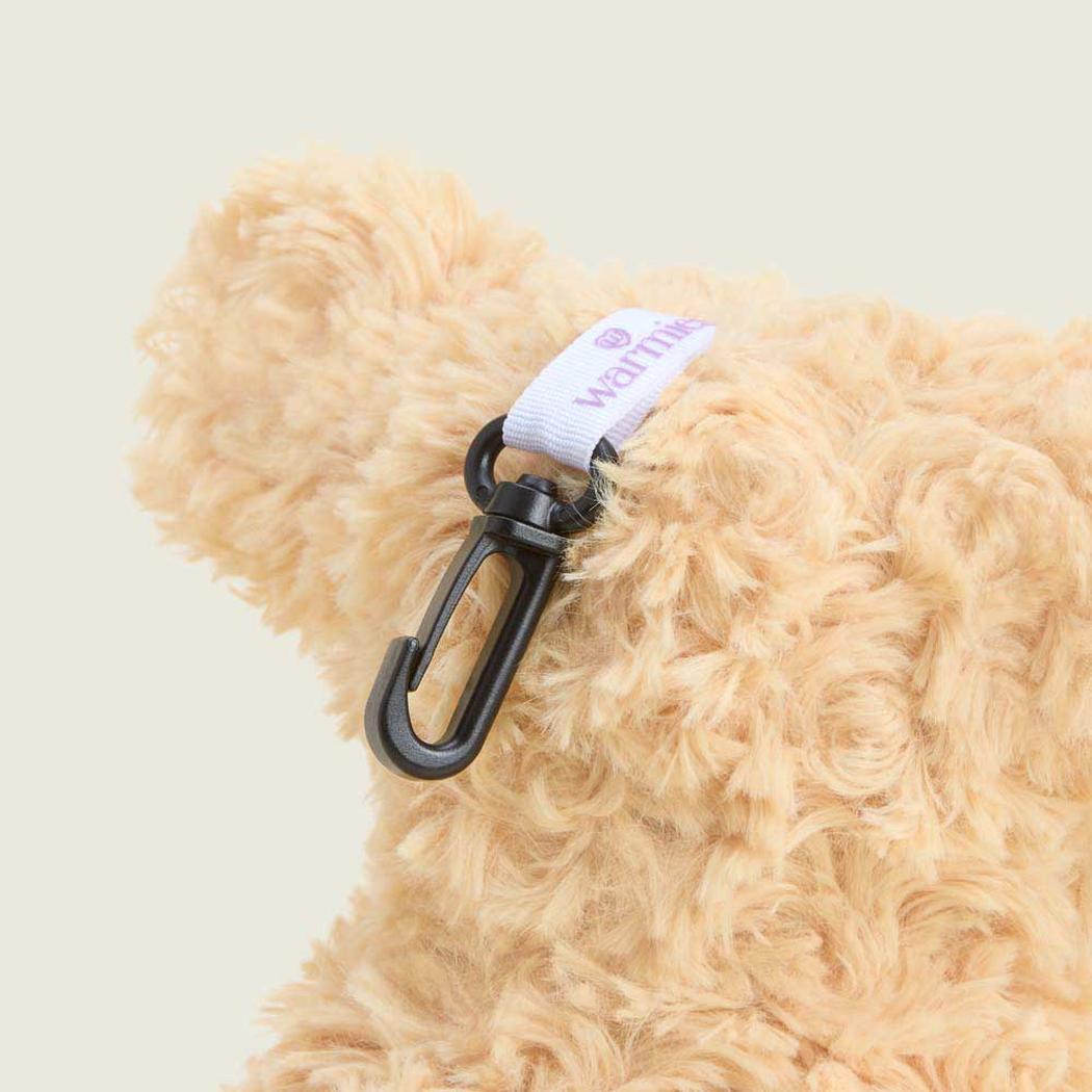 A close-up of the Warmies Curly Dog Bag Charm attached to a black carabiner on a light brown, curly stuffed animal.