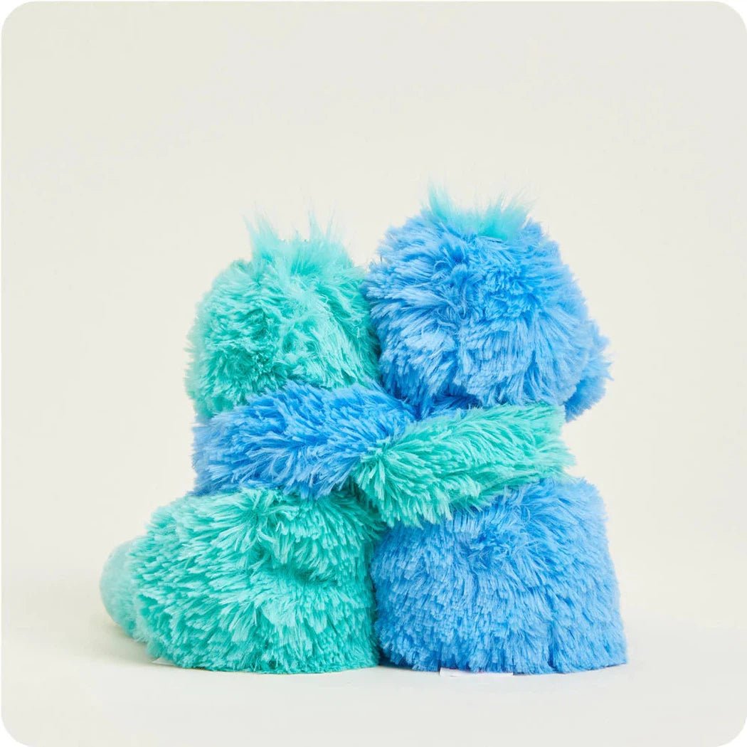 Two Warmies Dinosaur Hugs in blue and teal are shown from a front angle against a plain white background.