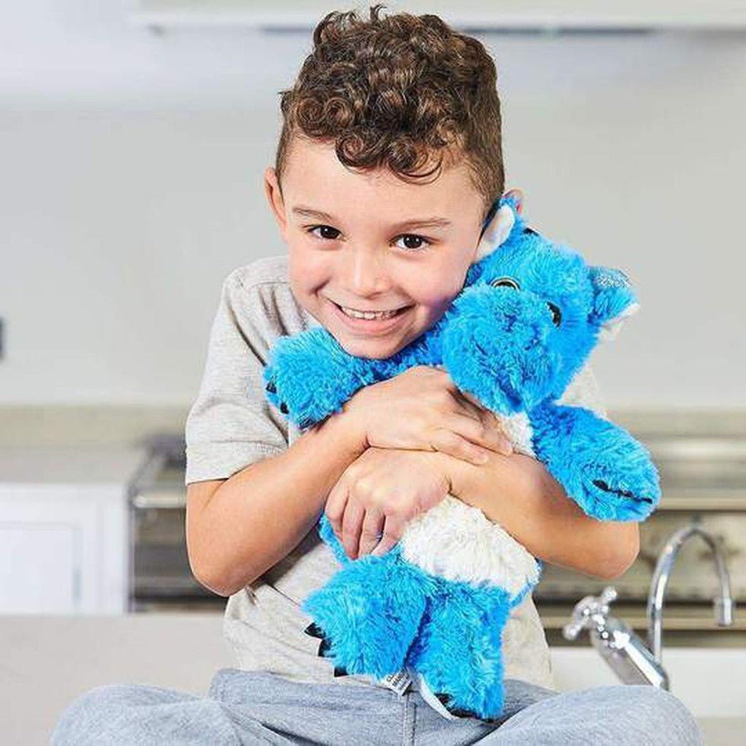 A young boy sits on a kitchen counter hugging a blue and white Warmies Dragon stuffed animal.