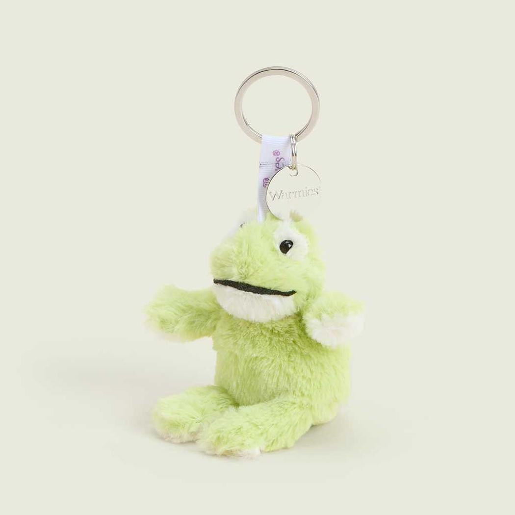 A close-up of the Warmies Frog Keyring, a light green plush frog with white accents, hanging from a silver keyring against a plain white background.