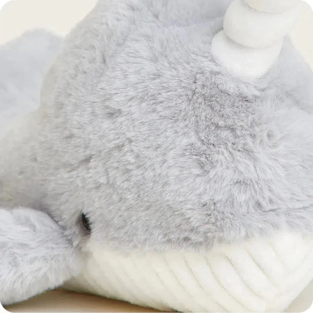 Close-up of the Warmies Narwhal showing its soft gray fur and white tusk against a light background.