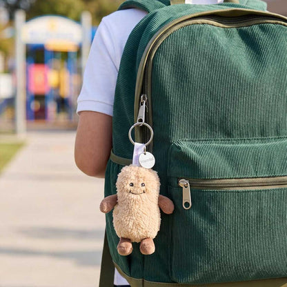 Back view of the Warmies Peanut Keyring attached to a green backpack with a playground in the background.